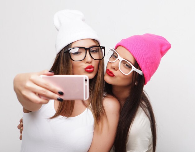 Due amici di ragazze adolescenti in attrezzatura hipster fanno selfie su un telefono