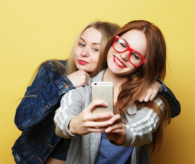 Due amici di ragazze adolescenti in attrezzatura hipster fanno selfie su un telefono