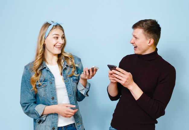 Due amici felici che sono eccitati con i telefoni nelle loro mani isolati su uno sfondo blu