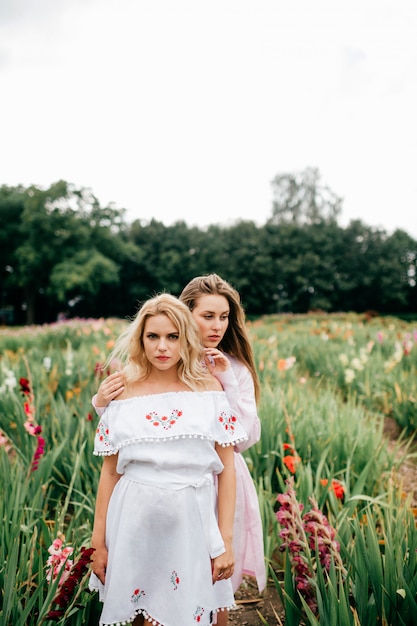 Due amici femminili abbastanza giovani in vestiti etnici che si rilassano nel giardino floreale di estate.