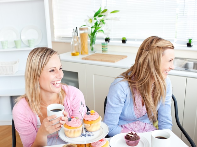 Due amici femminili che ridono mangiando dolci e bevendo caffè in cucina