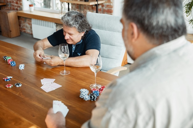 Due amici maturi felici che giocano a carte e bevono vino