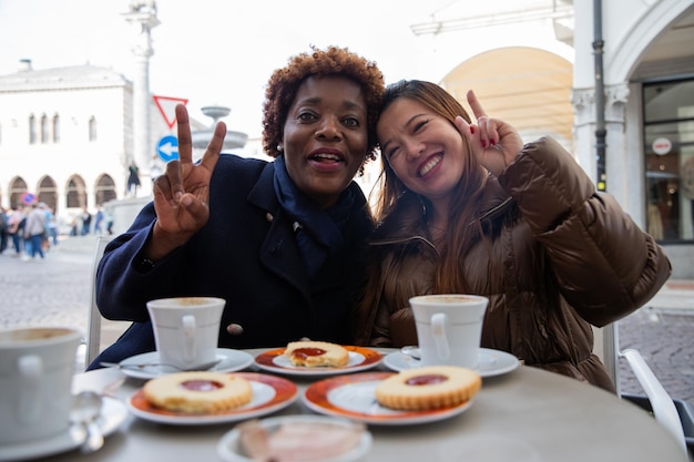 Due amici multirazziali sorridenti si godono la colazione facendo un segno di vittoria