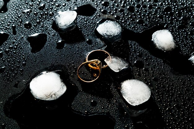 Due anelli dorati su sfondo nero con gocce d'acqua e pezzi di ghiaccio