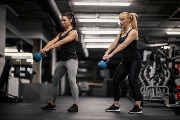 Due atleti muscolosi stanno facendo oscillare i kettlebell in una palestra