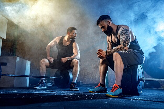 Due atleti tatuati barbuti muscolosi si rilassano dopo l'allenamento, sollevando pesi pesanti