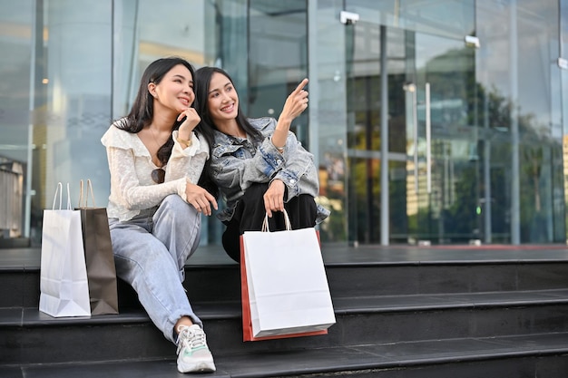 Due attraenti asiatici seduti sulle scale davanti all'ingresso del centro commerciale con le loro borse della spesa