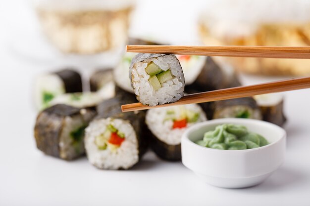 Due bacchette tenendo Hosomaki roll con verdure e diversi rotoli di sushi con frutti di mare