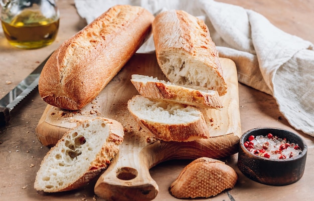 Due baguette francesi fatte in casa e una fetta tagliata su tagliere di legno su fondo rustico marrone Fuoco selettivo