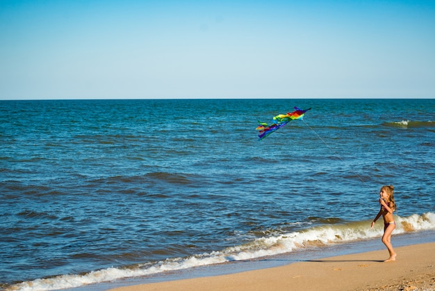 Due bambine allegre felici corrono con un aquilone sulla riva sabbiosa in riva al mare