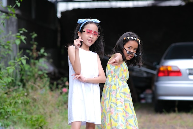 Due bambine asiatiche in posa insieme ai loro occhiali da sole giocattolo nel cortile sul retro