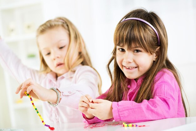 Due bambine carine che fanno gioielli di perline a casa