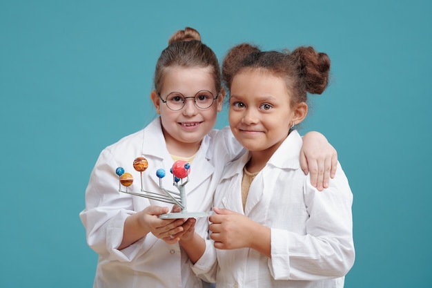 Due bambine carine in camice bianco con in mano modellini di piccoli pianeti