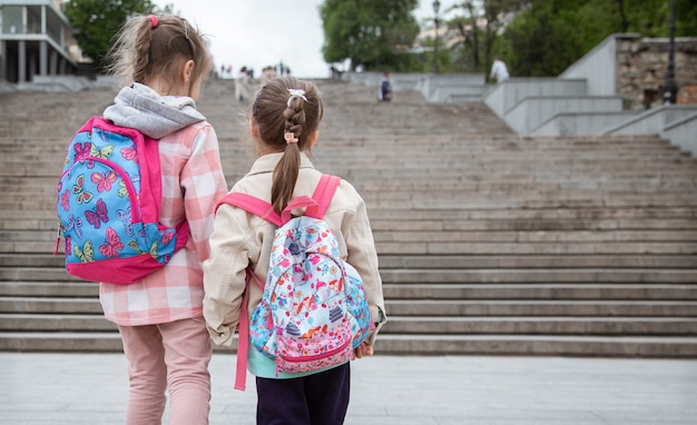 Due bambine con bellissimi zaini sulle spalle vanno a scuola insieme mano nella mano.
