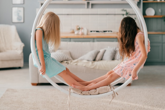 Due bambine con i capelli lunghi che coprono i loro volti seduti a swing nella stanza