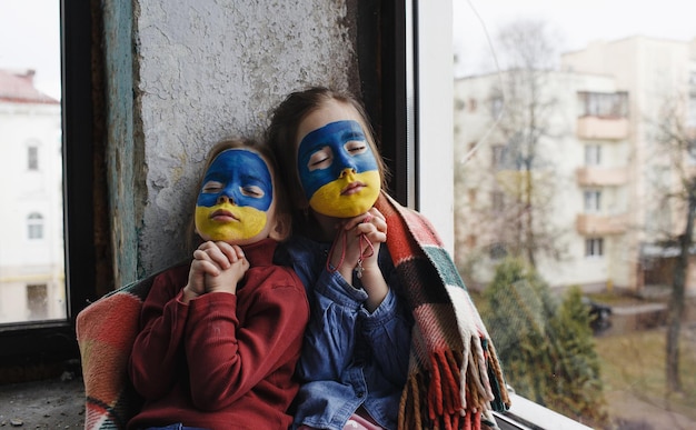 Due bambine con le bandiere ucraine dipinte sul viso stanno pregando per l'Ucraina un gesto di fede e speranza I bambini sono contrari alla guerra