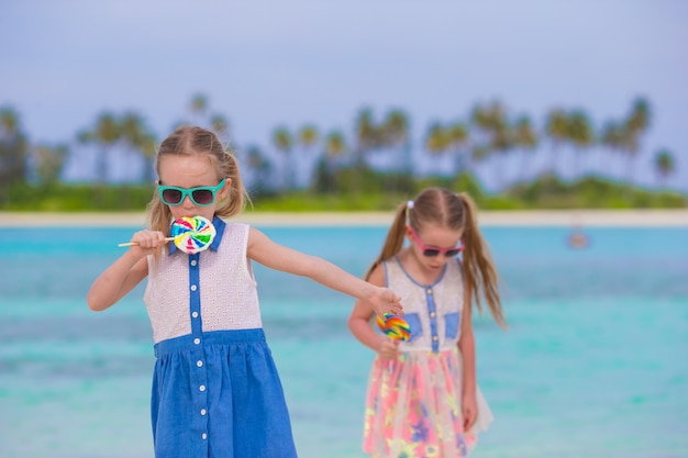 Due bambine con lecca-lecca gustose luminose sulla spiaggia bianca