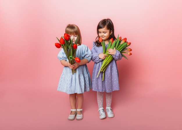 Due bambine con un mazzo di tulipani su sfondo rosa