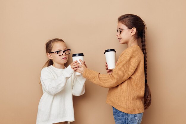 Due bambine divertenti un bicchiere con una bevanda sfondo beige