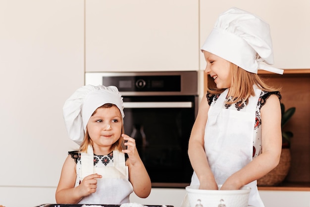 Due bambine felici in cappelli da chef giocano con la farina in cucina