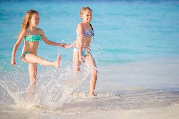 Due bambine felici si divertono molto in spiaggia tropicale giocando insieme in acque poco profonde.