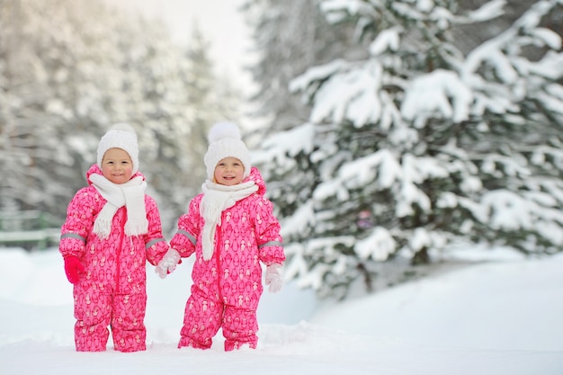 Due bambine gemelle vestite di rosso stanno in una foresta invernale innevata.