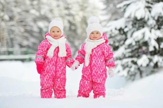 Due bambine gemelle vestite di rosso stanno in una foresta invernale innevata.