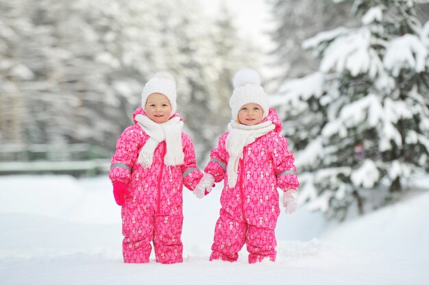 Due bambine gemelle vestite di rosso stanno in una foresta invernale innevata.