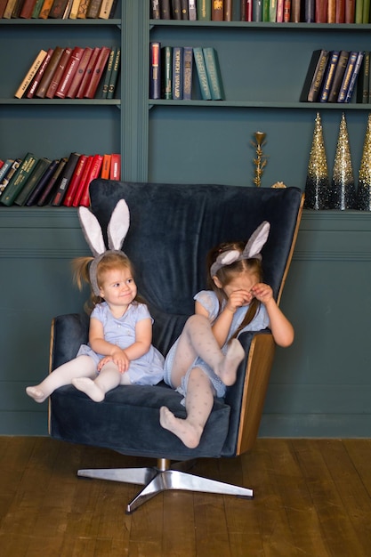 Due bambine in costume da coniglio simbolo del 2023 su una sedia vicino agli alberi di Natale