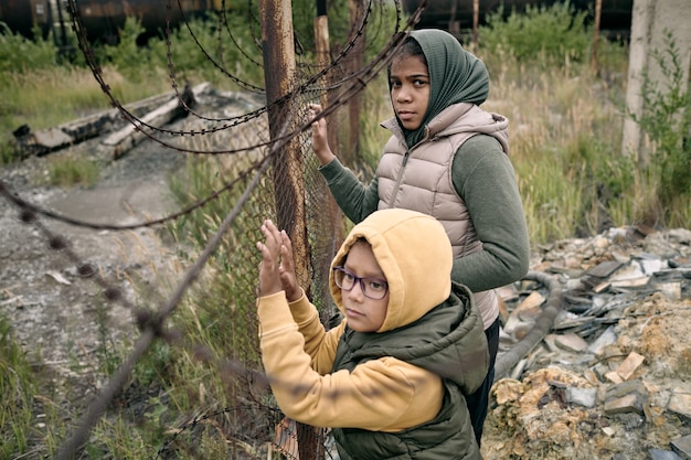 Due bambine in felpe con cappuccio e giacche in piedi accanto alla rete che divide il campo profughi