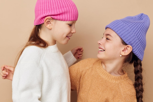 Due bambine in maglioni e cappelli abbracciano amicizia sfondo beige