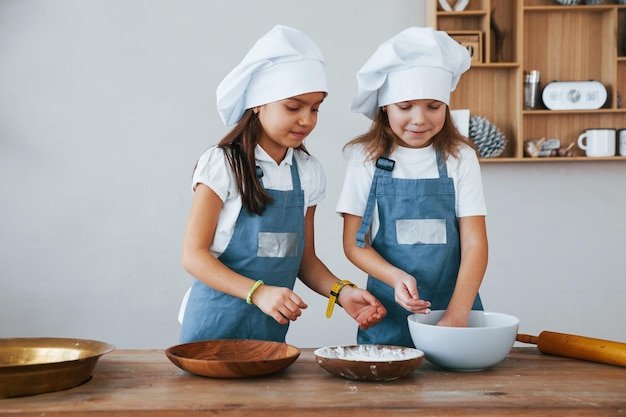 Due bambine in uniforme blu da chef che lavorano con la farina in cucina