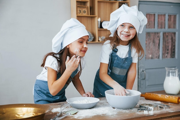 Due bambine in uniforme blu da chef si divertono con la farina in cucina