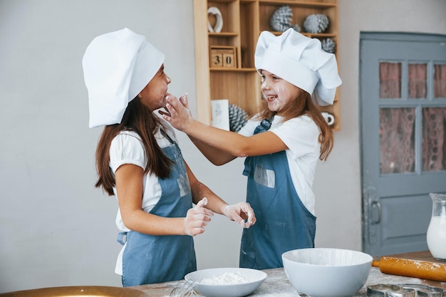 Due bambine in uniforme blu da chef si divertono con la farina in cucina