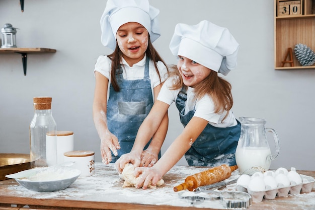 Due bambine in uniforme blu dello chef che impastano la pasta in cucina