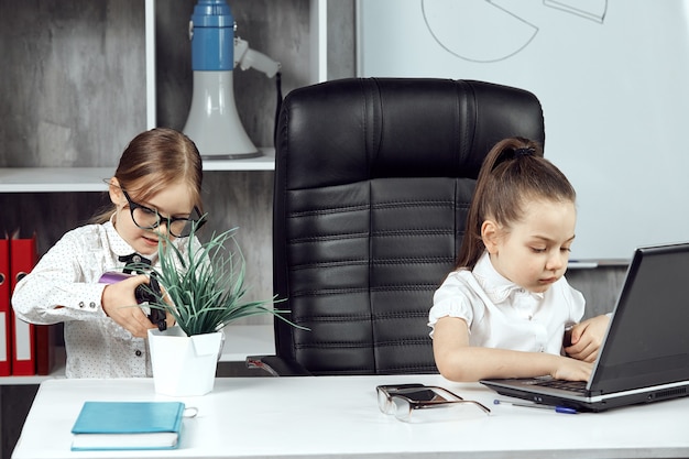 Due bambine posano come impiegati che lavorano su un laptop e innaffiano fiori