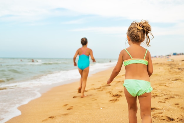 Due bambine positive corrono lungo la spiaggia di sabbia in una soleggiata giornata estiva calda