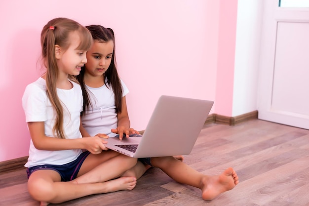 Due bambine sedute davanti a un laptop e ridono, primo piano, emozioni positive, intrattenimento su Internet per bambini