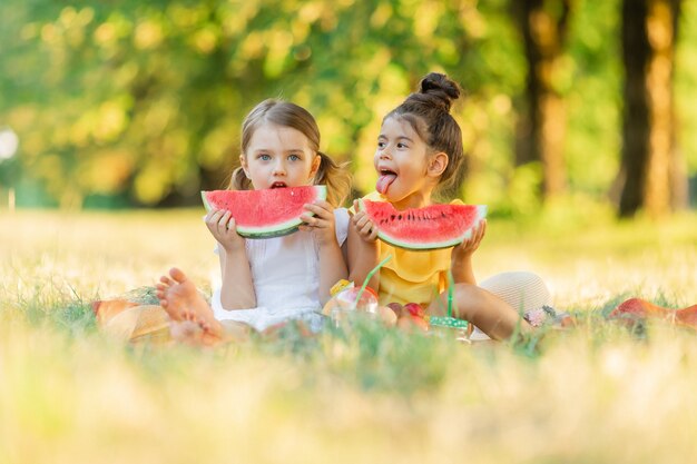 Due bambine si divertono a giocare a mangiare un pezzo di frutta di anguria all'aperto