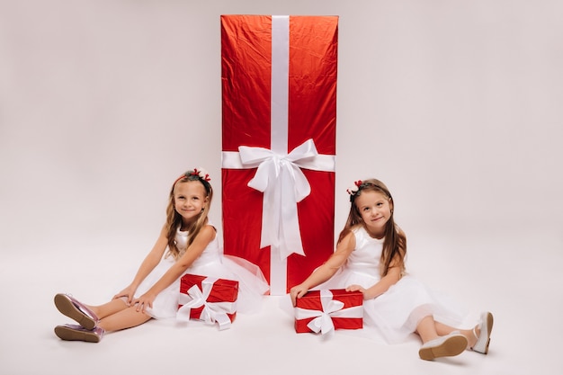 Due bambine si siedono con i regali di Natale su uno sfondo bianco e un regalo enorme.