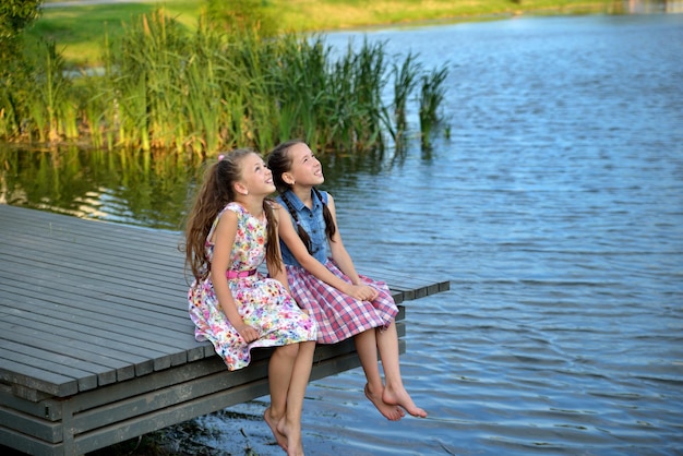 Due bambine si siedono su un ponte di legno vicino al fiume al tramonto e guardano il cielo