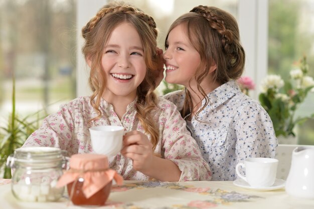 Due bambine sorridenti che bevono tè a casa