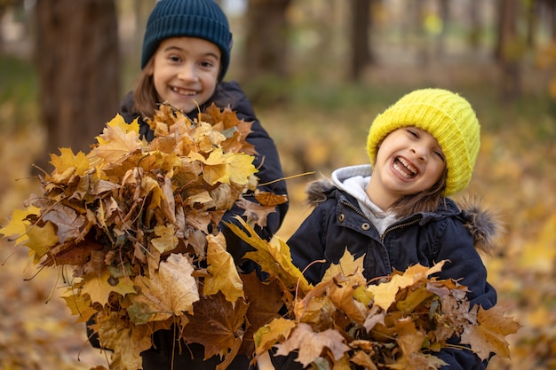 Due bambine stanno giocando tra le foglie d'autunno per una passeggiata nella foresta