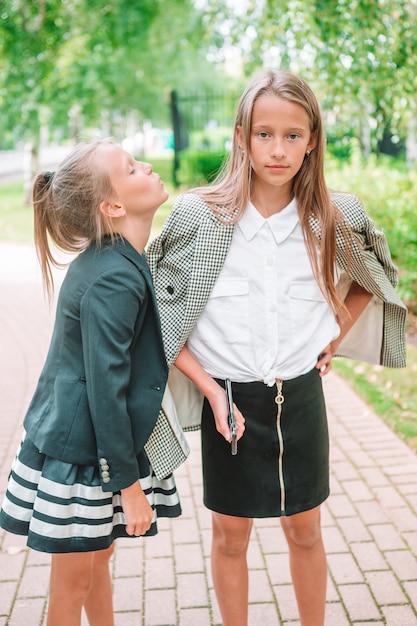 Due bambine sveglie in posa davanti alla loro scuola. Adorabili bambini piccoli che si sentono molto entusiasti di tornare a scuola