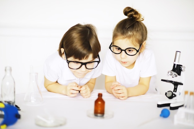 Due bambini carini alla lezione di chimica che fanno esperimenti isolati su sfondo bianco