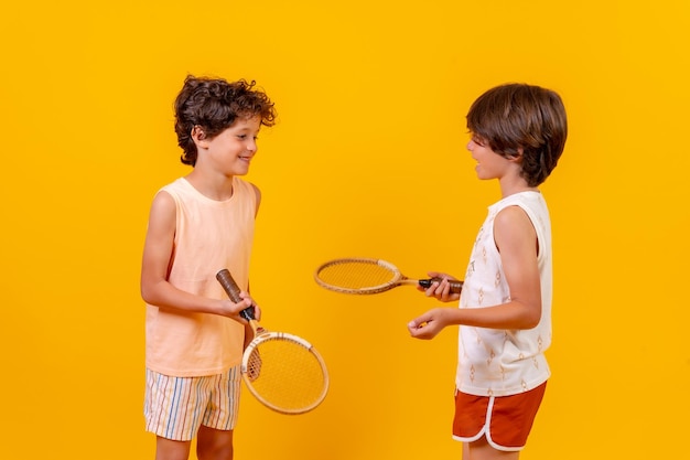 Due bambini che giocano a tennis e si divertono su sfondo giallo