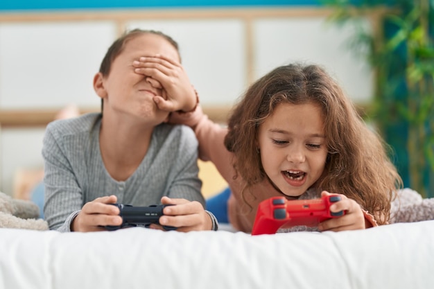 Due bambini che giocano al videogioco sdraiati sul letto che tradiscono in camera da letto