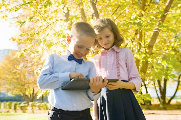 Due bambini che guardano compressa digitale, parco soleggiato di autunno del fondo