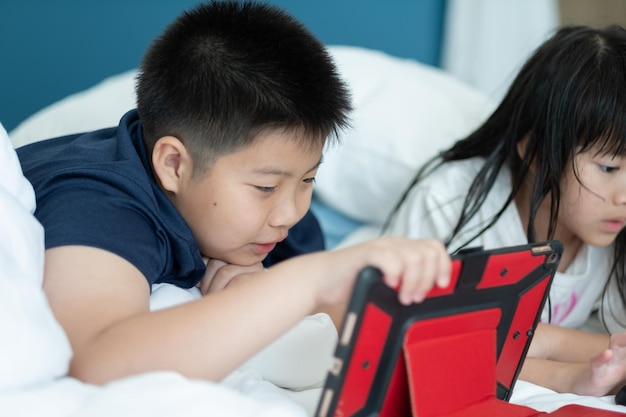 Due bambini cinesi addicted tablet bambino asiatico guardando il telefono insieme sul loro letto bambino utilizzando smartphone