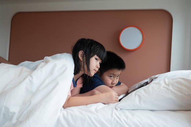 Due bambini cinesi dipendenti tablet asiatico bambino che guarda il telefono insieme sul loro letto bambino utilizzando smartphonexA